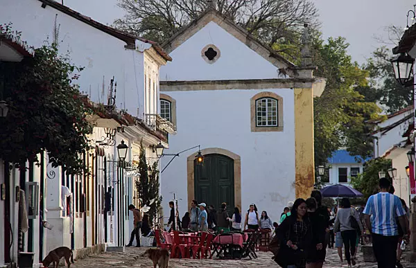 Rua de Paraty com mesas ao ar livre e a Igreja de Santa Rita ao fundo, com visitantes passeando